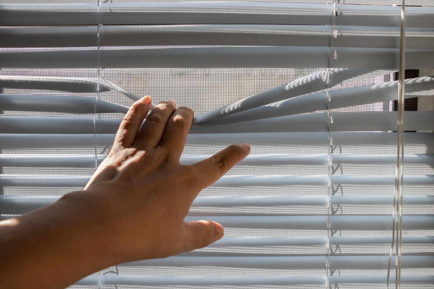 Hand bedient den Schnurzug eines Fenster-Sonnenschutzes