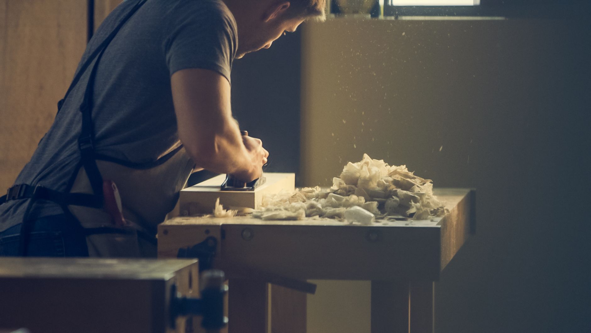 Werkbank selber bauen – Handwerker hobelt Holz an einer massiven Werkbank