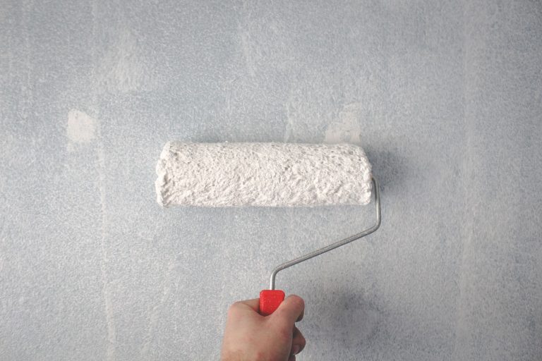 Silikatfarbe auf Dispersionsfarbe streichen: Geht das? Silikatfarbe auf Dispersionsfarbe – Farbrolle trägt weiße Wandfarbe auf eine Innenwand auf