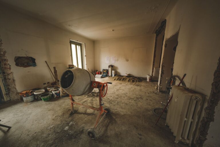 Beton abschleifen – Renovierungsraum mit rohem Estrichboden, Betonmischer und Werkzeug