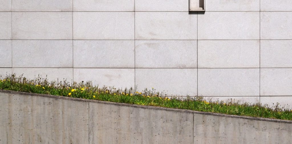 Glatte Sichtbeton-Stützwand fängt einen begrünten Hang vor einer Gebäudefassade ab