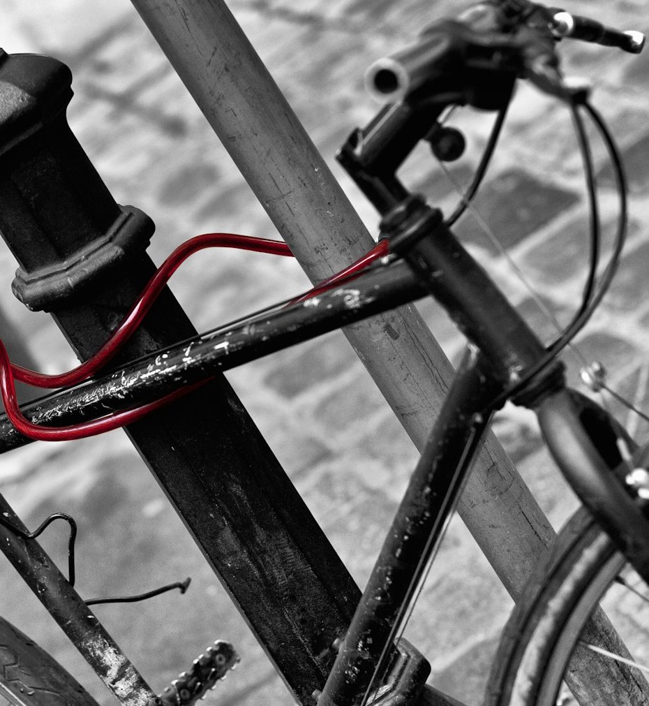 Fahrrad mit rotem Kabelschloss an einem Poller auf Kopfsteinpflaster